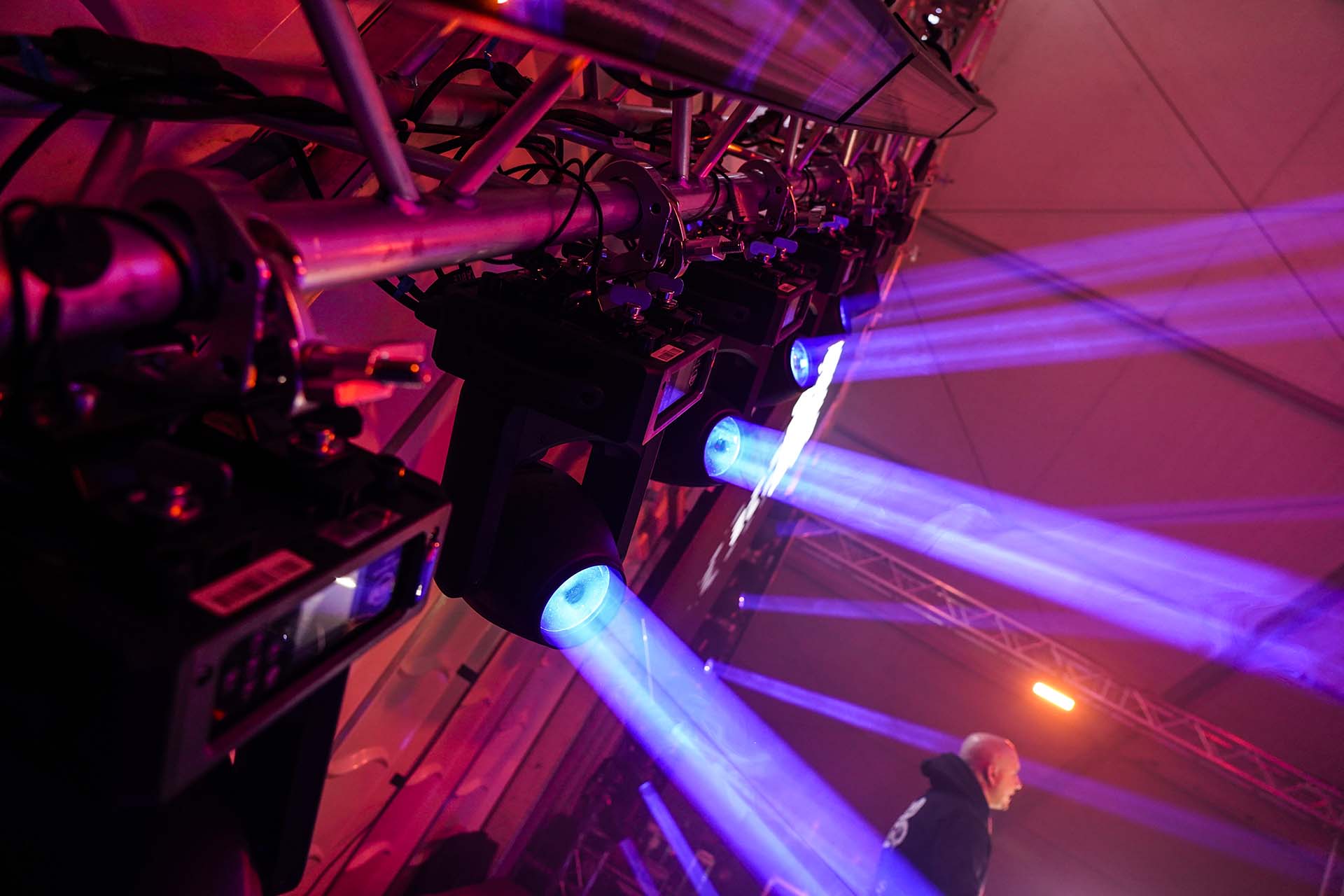 Mehrere blau leuchtende Moving Heads an einer Traverse montiert mit rot beleuchteter Bühne.