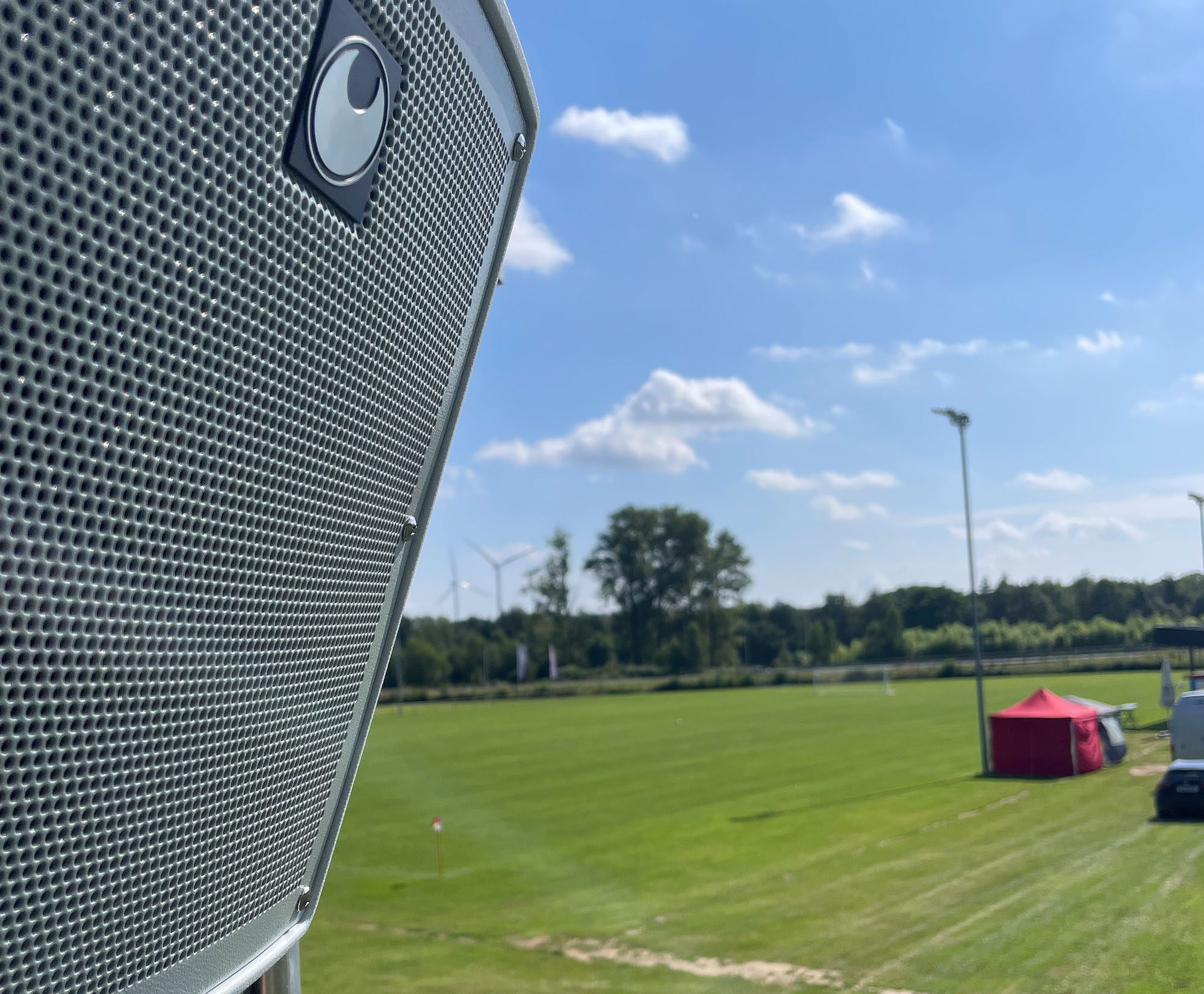 Lautsprecher auf einem Sportfeld mit Rasenplatz im Hintergrund.