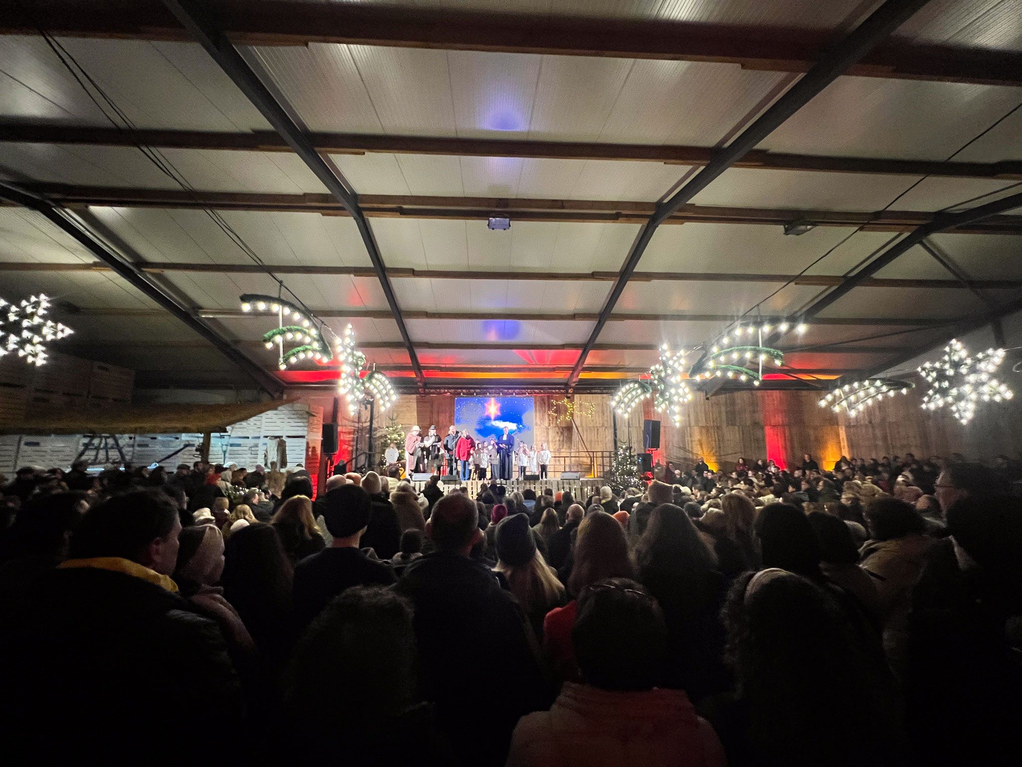 Große Menschenmenge vor einer weihnachtlich geschmückten Bühne mit Kindern und einem Sänger.