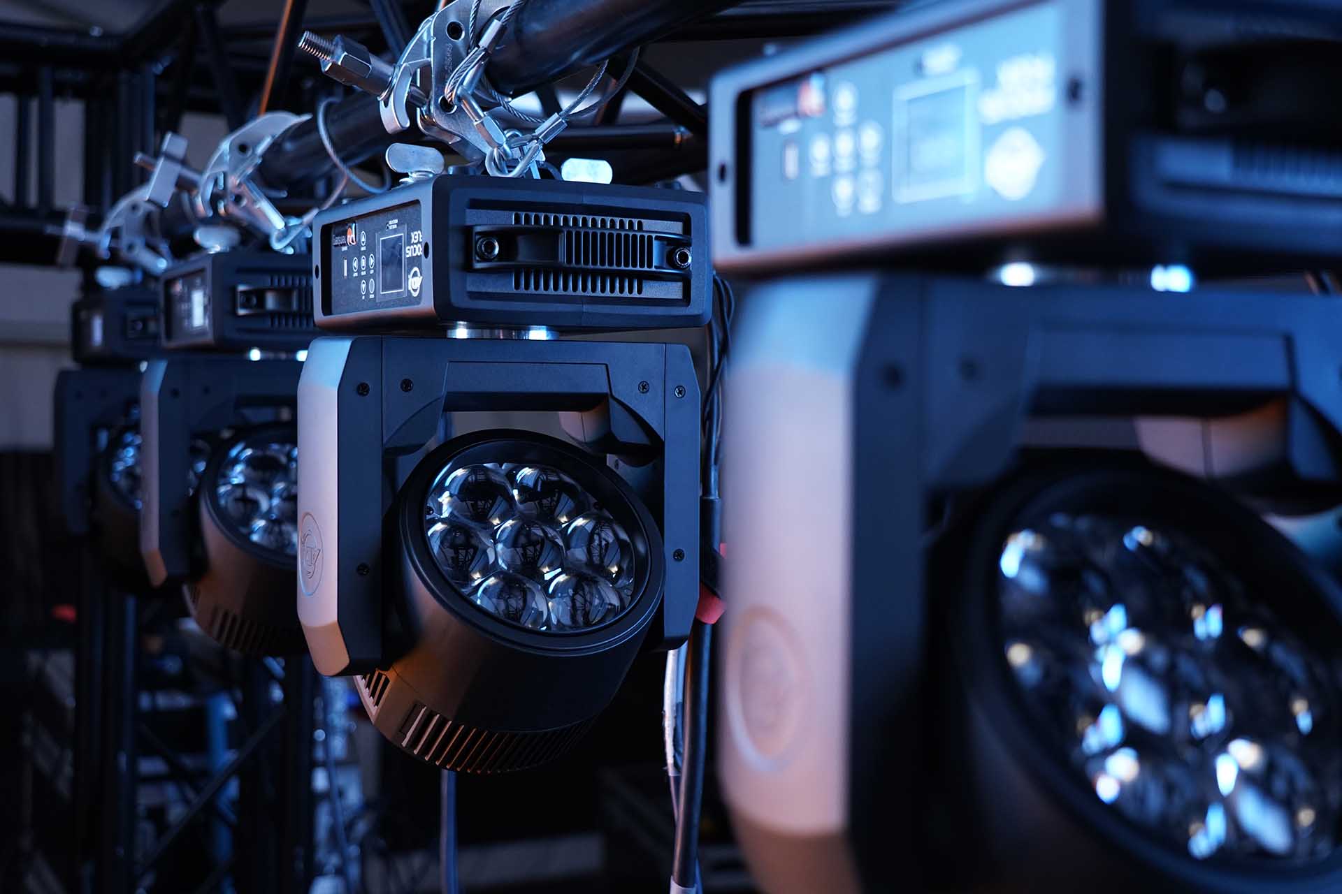 Vier LED Moving Heads hintereinander an einer schwarzen Traverse montiert.