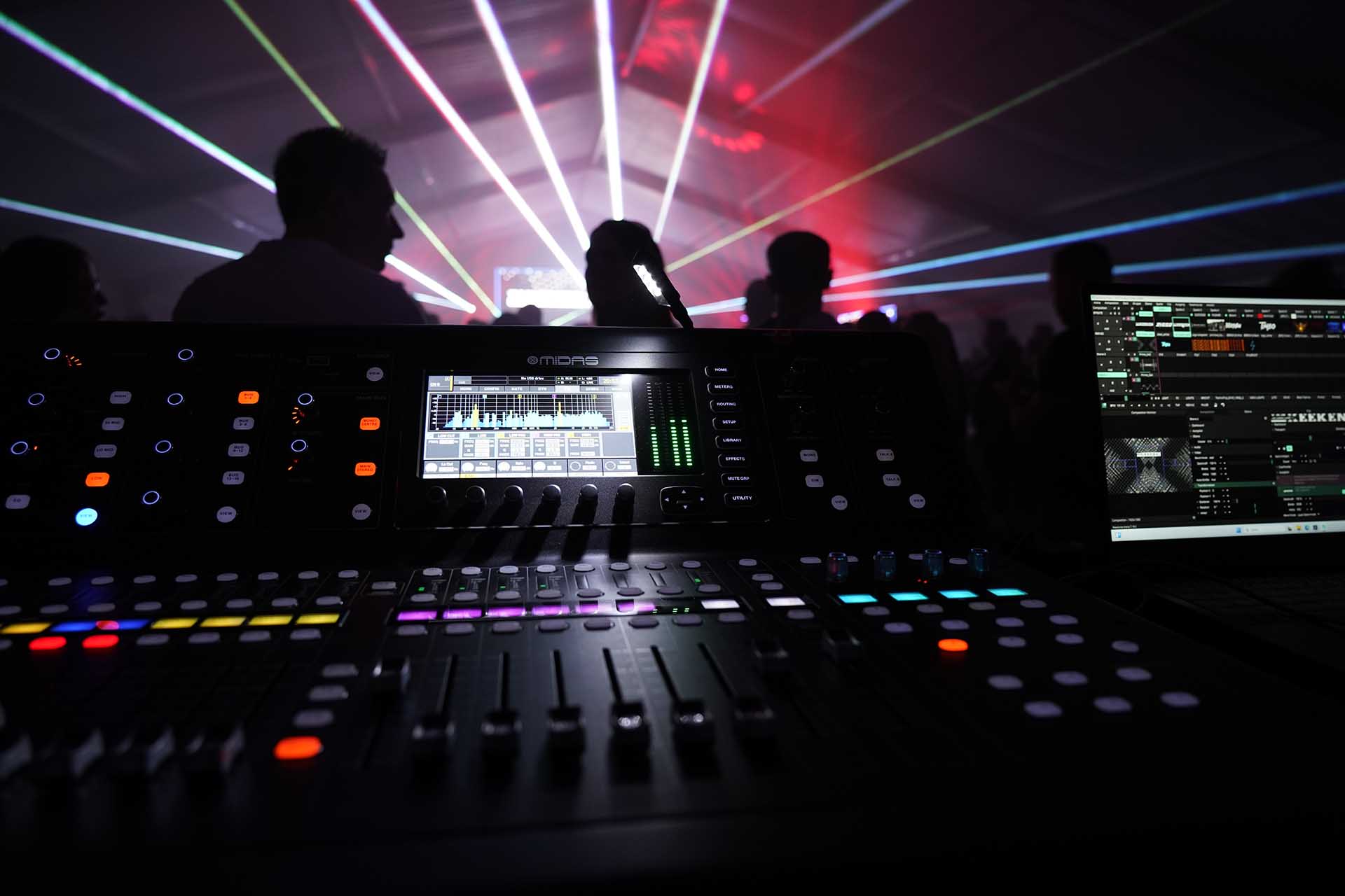 Tontechnik Mischpult mit Silhouetten von Leuten und Laserstrahlen im Hintergrund.