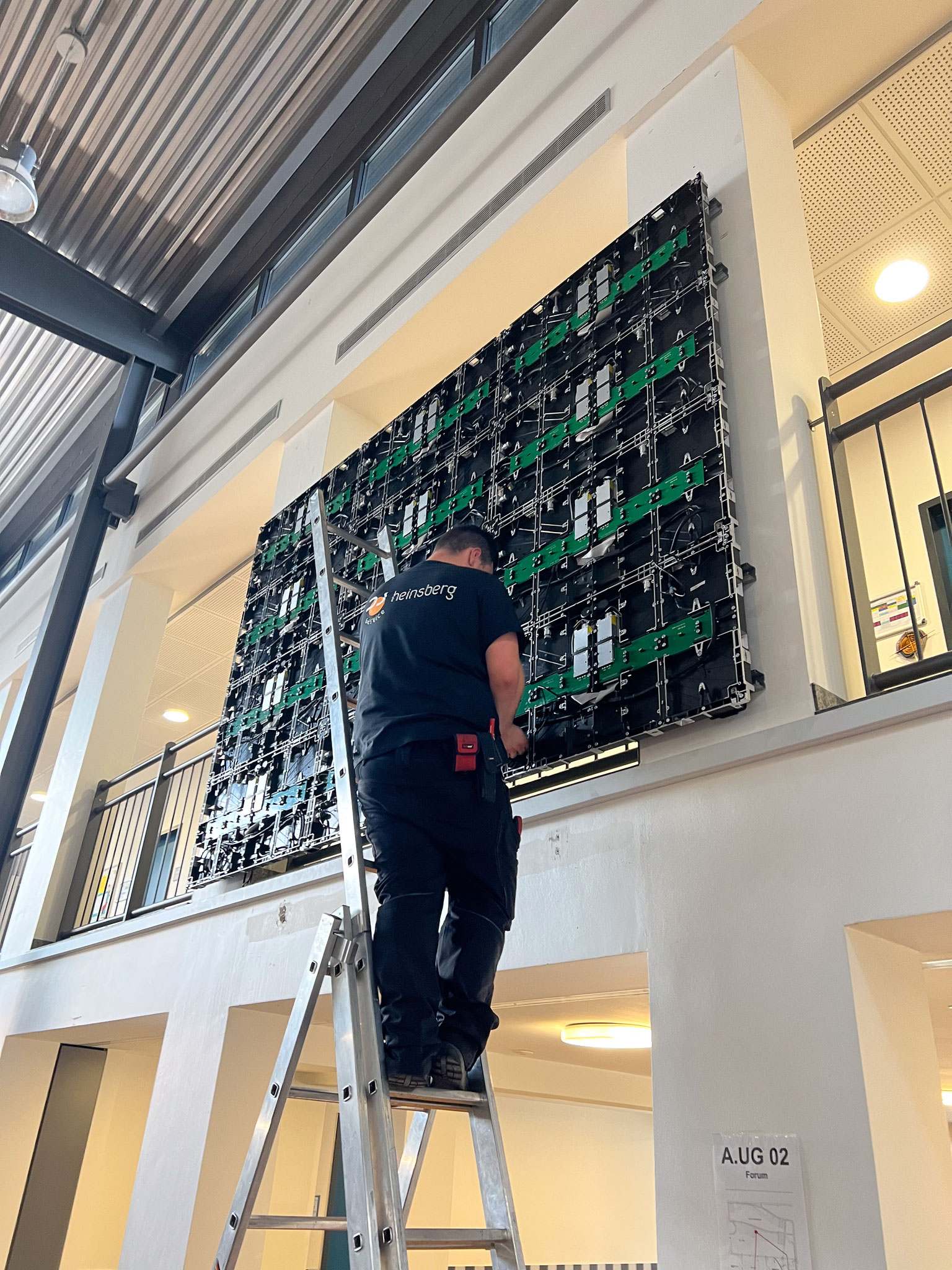 Techniker montiert eine LED-Wand in einer Aula und steht auf einer Leiter.
