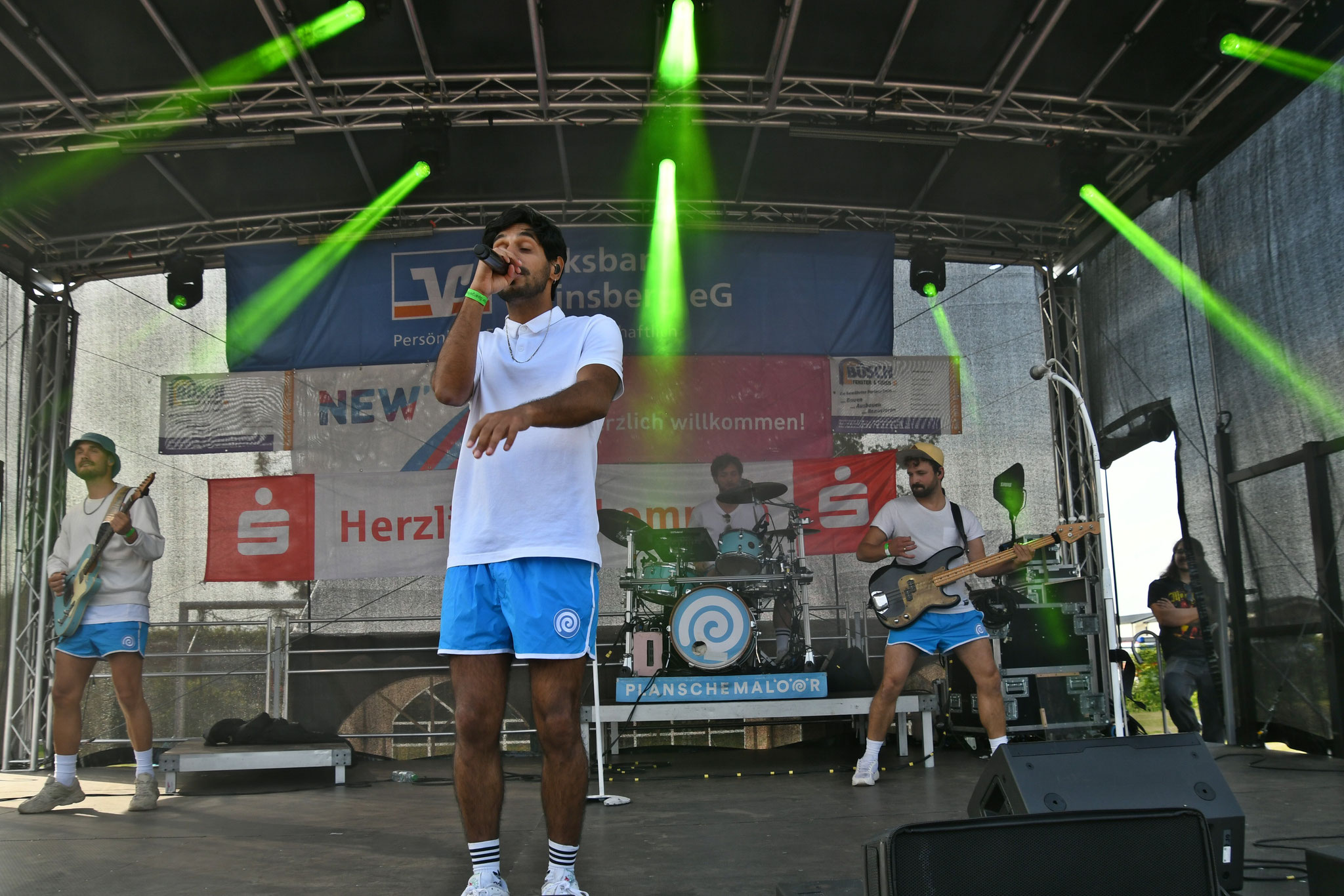 Sportlich gekleidete Band mit Sänger und grünem Licht in einer Outdoor Bühne.