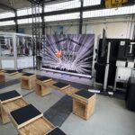 Technische Halle mit LED-Videowand und davor platzierten Sitzgelegenheiten zum Sitzen.
