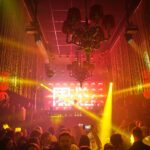 Gelb-rot beleuchteter Tanzclub mit Bühne und großer LED-Videowand im Hintergrund.