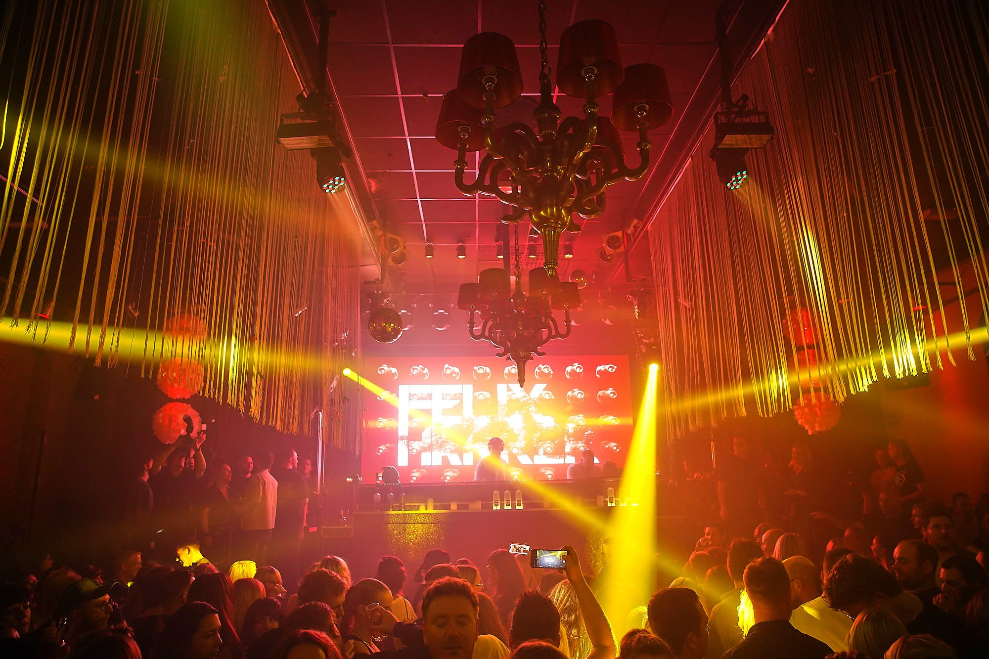 Gelb-rot beleuchteter Tanzclub mit Bühne und großer LED-Videowand im Hintergrund.