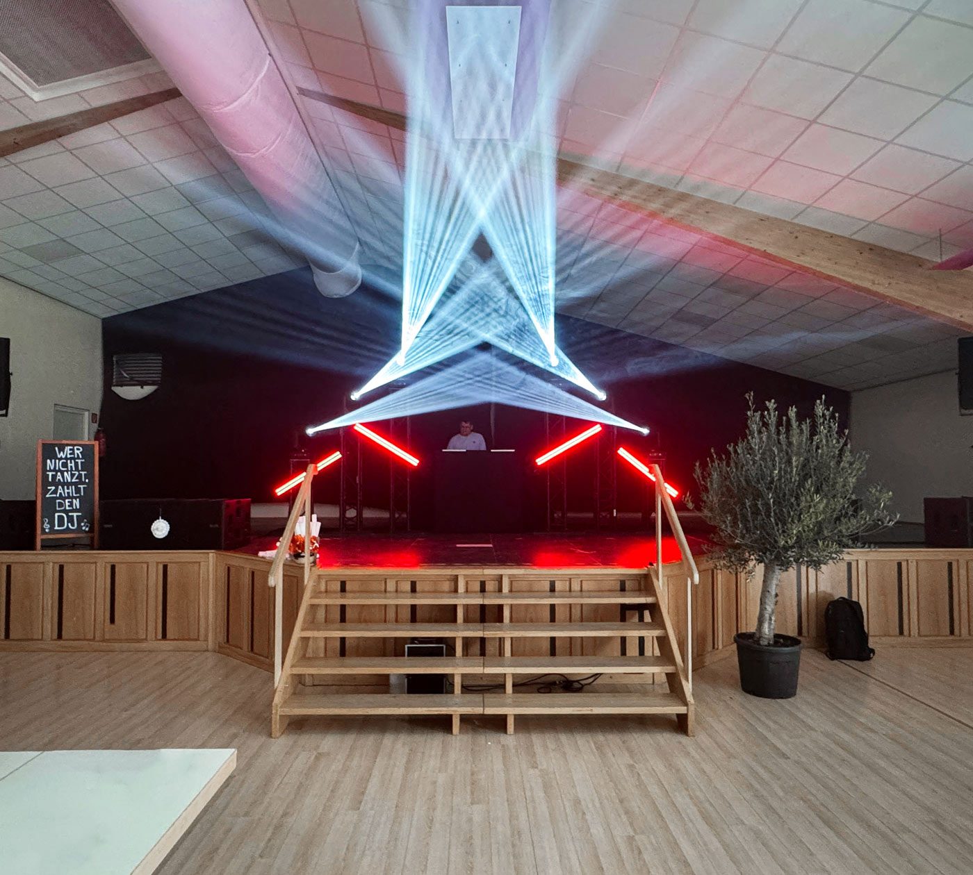 Saal mit DJ-Setup mit Moving Heads und rot leuchtenden LED-Bars.