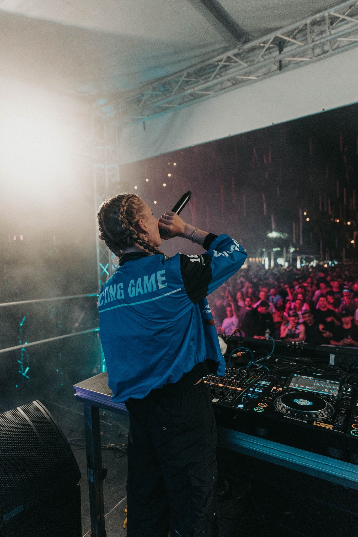 DJ mit Mikrofon auf der Bühne mit vielen Menschen im Hintergrund.