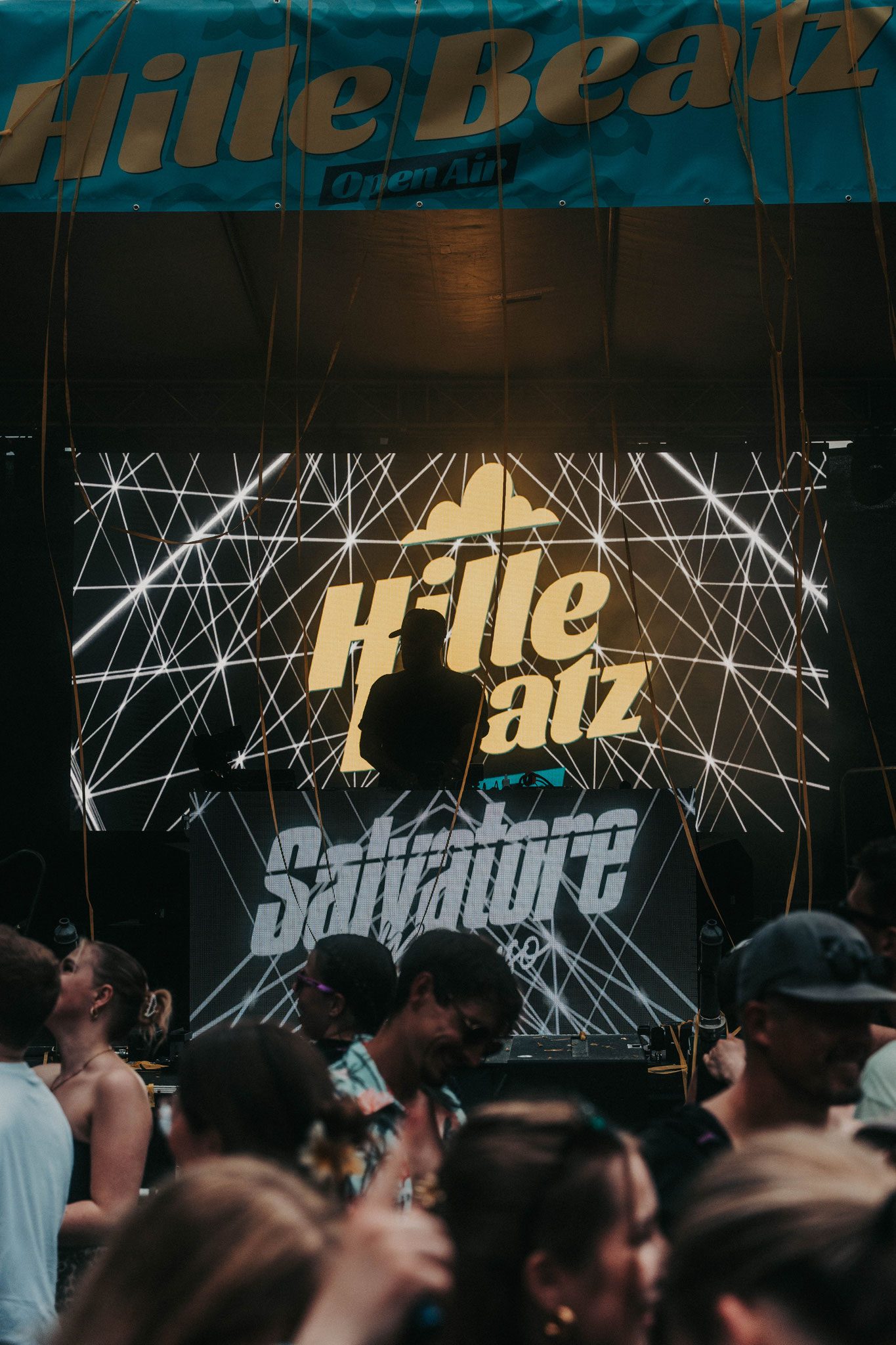 Nahaufnahme des DJ-Pultes mit DJ und LED-Videowand im Hintergrund.