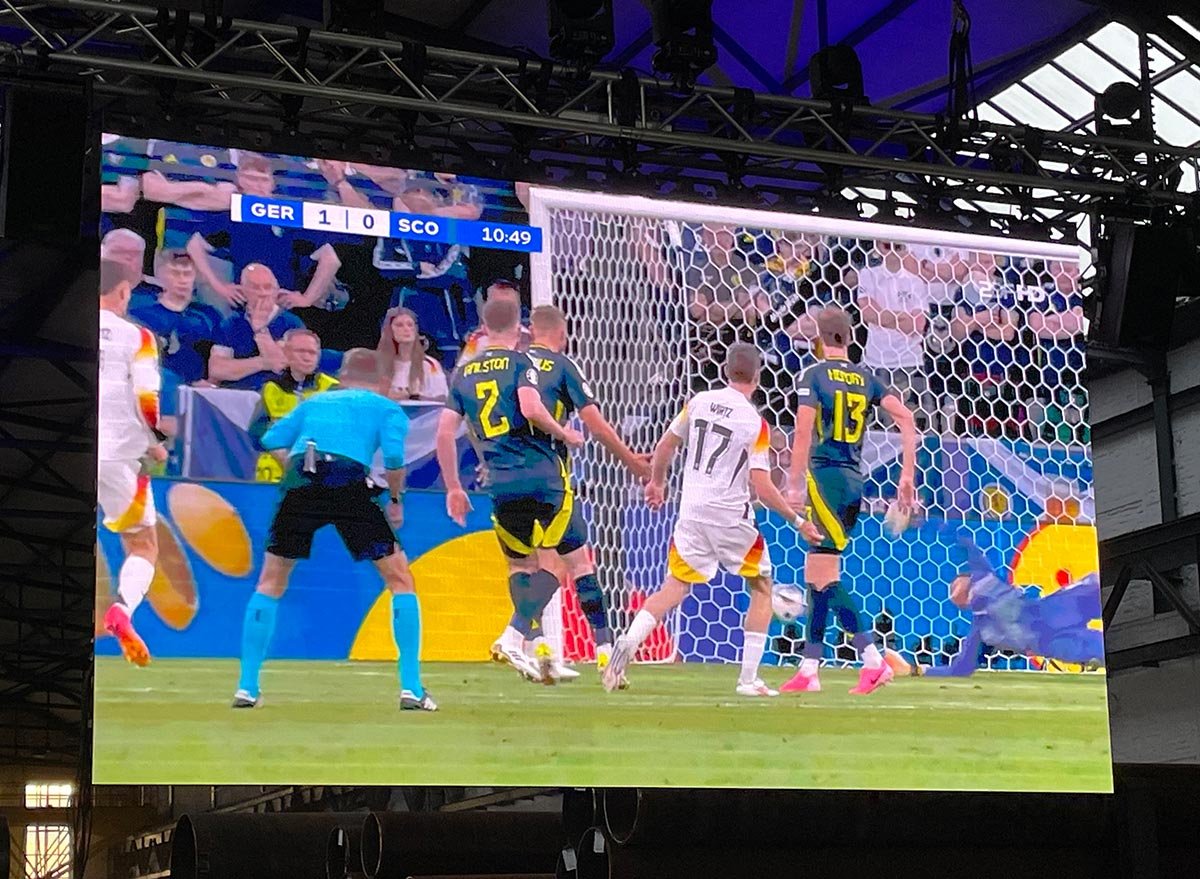 Live Übertragung eines Fußballspiels auf einer LED Videowand an der Decke einer Industriehalle mit Tor Szene.